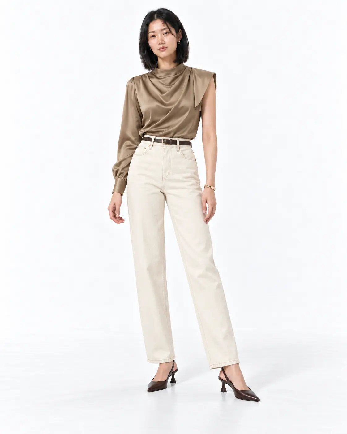 Modern Utility Layer Woman wearing a belted khaki utility jacket, ivory T-shirt, black ankle trousers and brown loafers in a white studio.