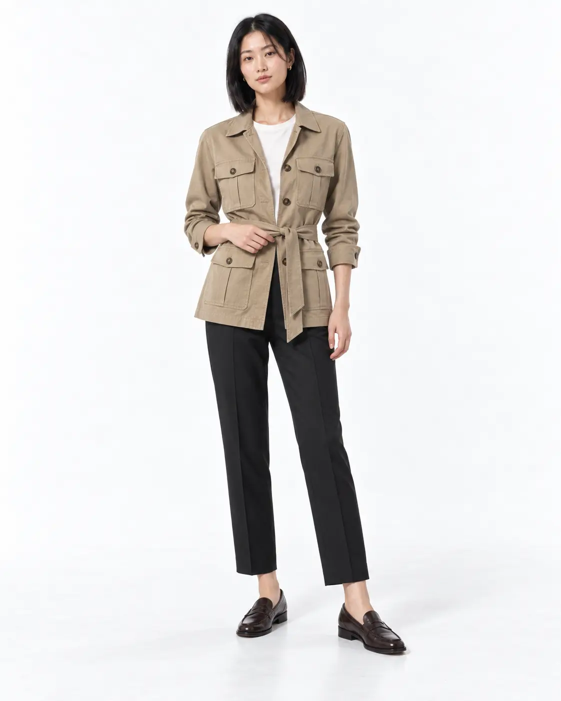 The Khaki Trench Dress Woman in a sleeveless belted khaki trench midi dress with burgundy ankle boots against a white studio background.