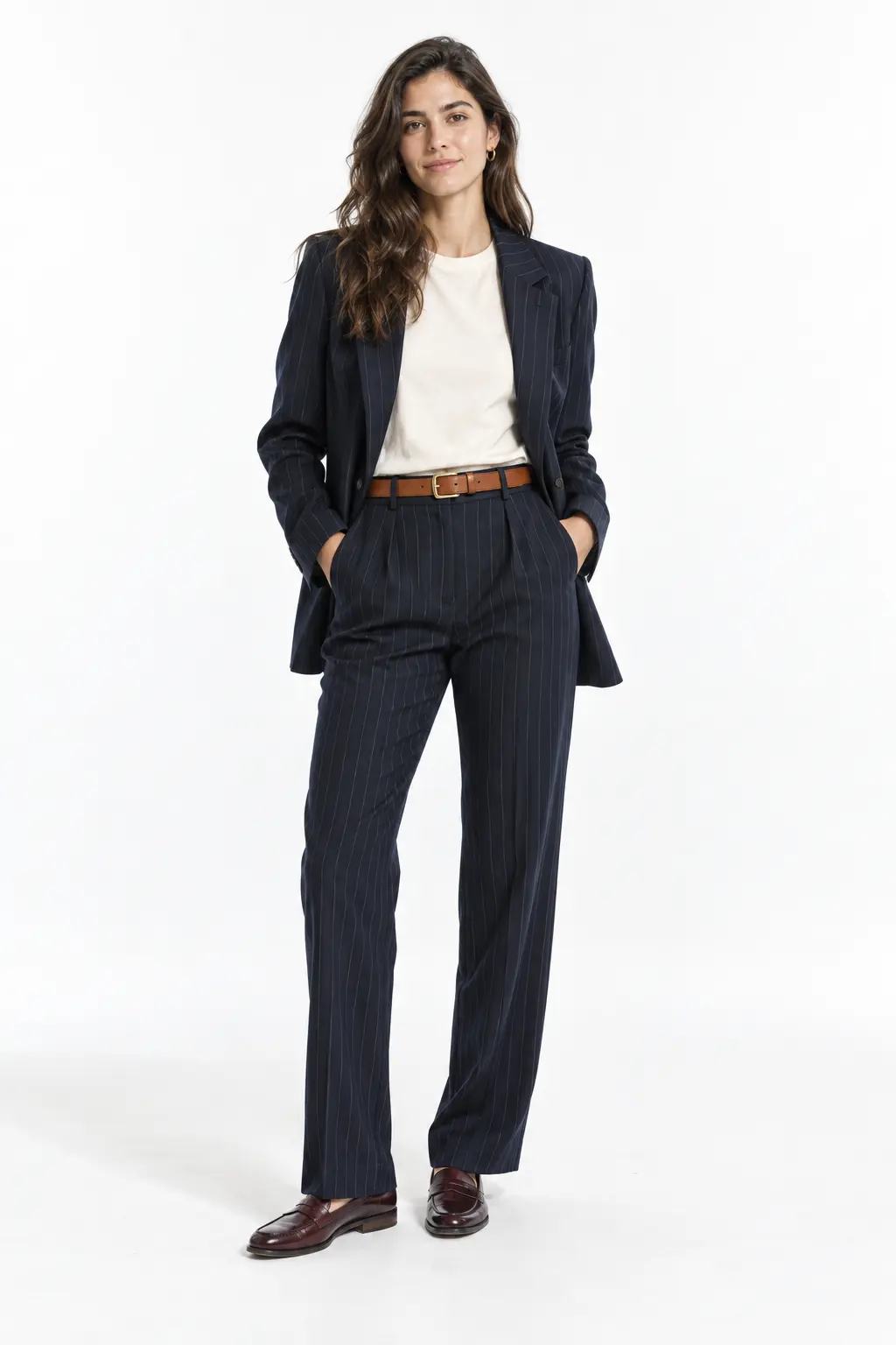 Navy Pinstripe Suit with Cream Tee Full-body white-studio image of a woman wearing navy pinstripe blazer and straight trousers; cream crew-neck T-shirt; oxblood loafers; tan belt.