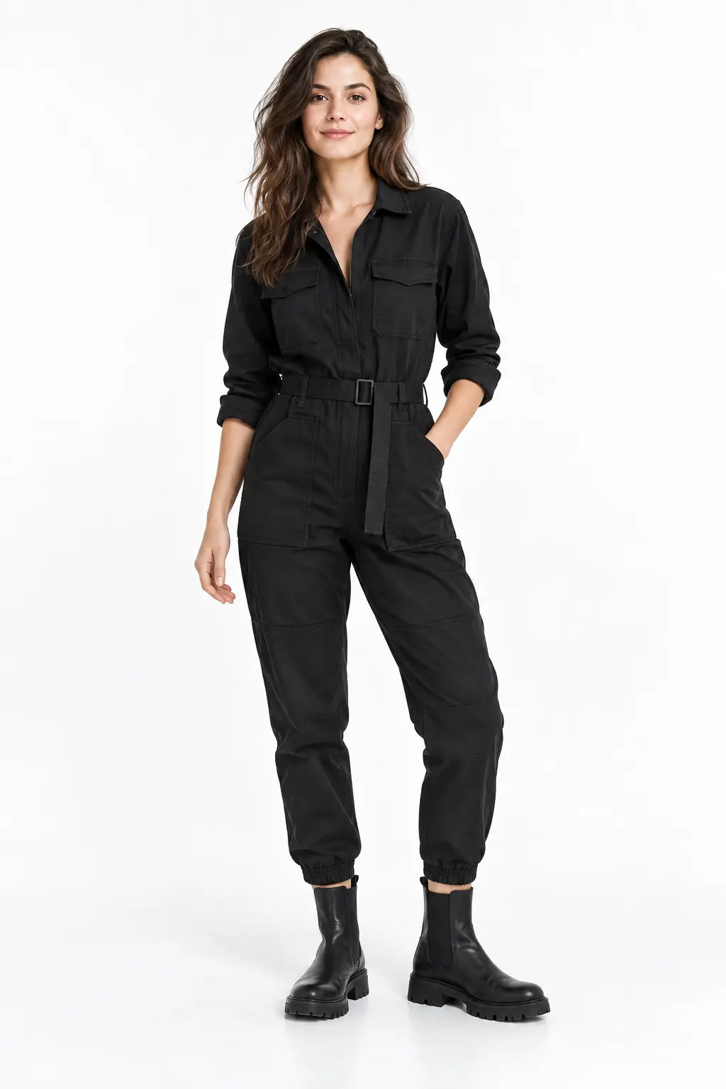 Black Utility Jumpsuit Full-body white-studio image of a woman wearing black belted utility jumpsuit; black lug Chelsea boots.
