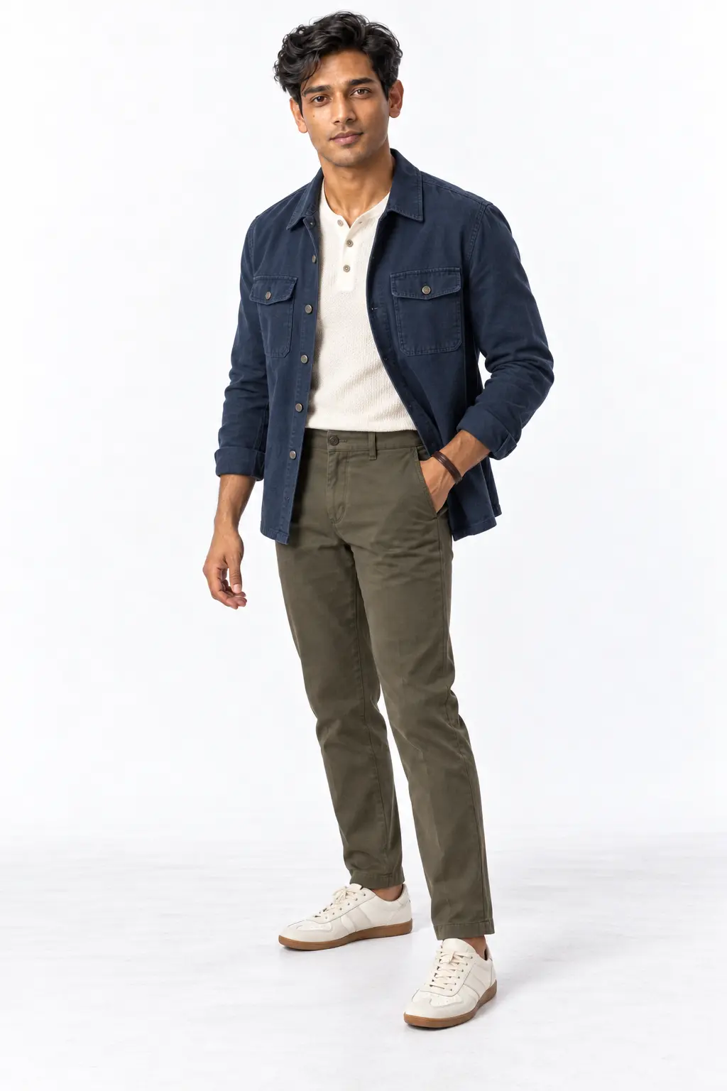 Indigo Overshirt Fall Outfit Man wearing a washed indigo overshirt, ecru henley, olive chinos and off-white sneakers in a white studio