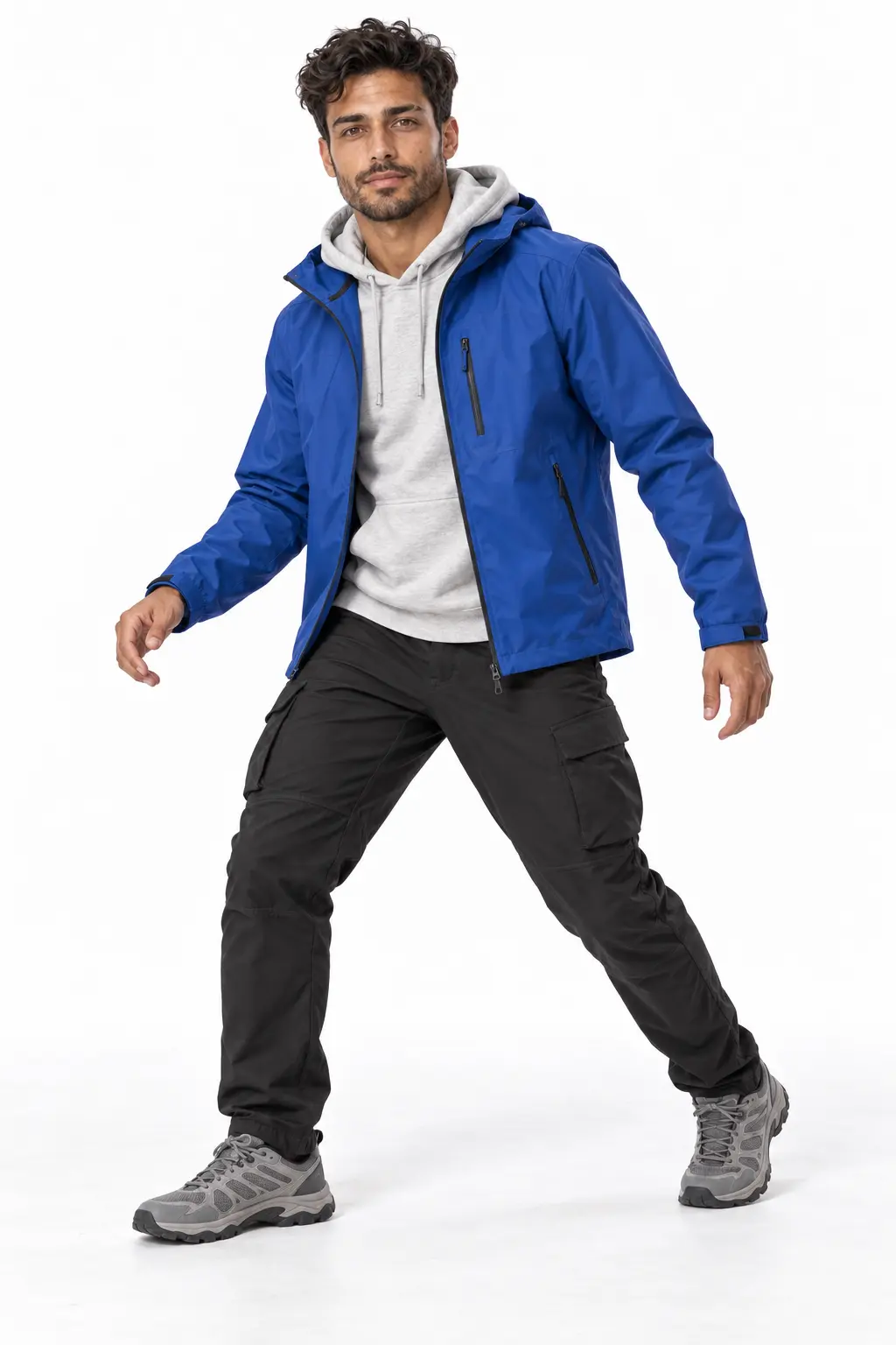 Men's Cobalt Shell Weekend Outfit A man posing in a cobalt blue shell jacket layered over a grey hoodie, paired with black cargo pants and grey hiking sneakers.