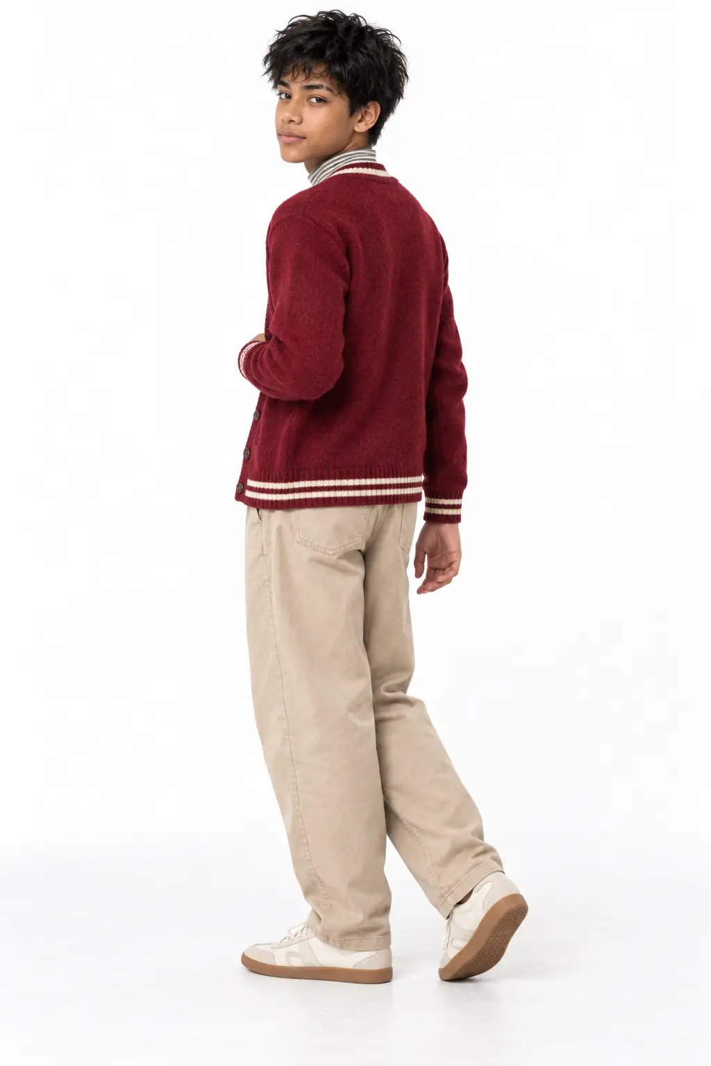 Teen Boy Looking Back in Berry Red Knit Cardigan and Beige Chino Pants Rear three-quarter view of a teenage boy looking over his shoulder, wearing a berry red knit cardigan with cream striped trim, relaxed-fit beige chino trousers, and white gum-sole sneakers.